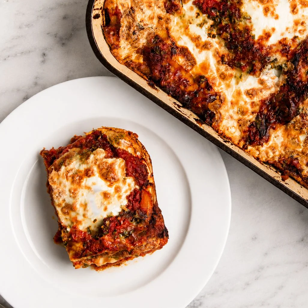 A single serving of eggplant Parmesan on a plate alongside a casserole dish with the rest of the eggplant parm.
