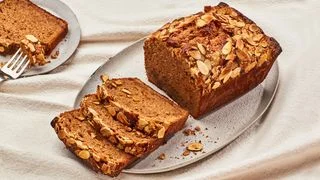 A loaf of almond butter quick bread topped with sliced almonds with several slices arranged on a platter and a fork...