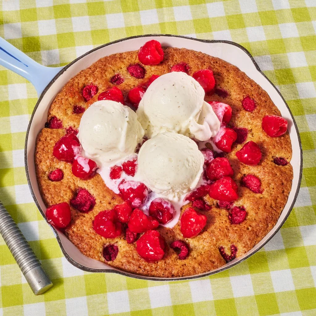 freshly baked RaspberryBrown Butter Skillet Cake topped with ice cream on a green gingham surface.