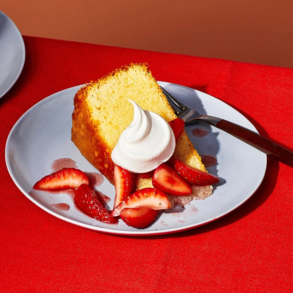 A slice of almond cake with a dollop of whipped cream and a side of strawberries.
