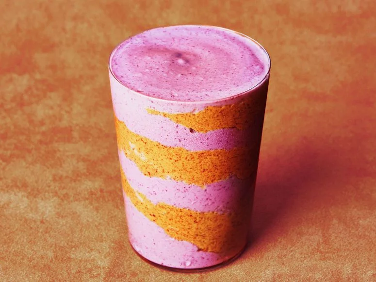 Blended mixed berries cottage cheese water and almond butter in a glass cup with a swirl of almond butter inside.