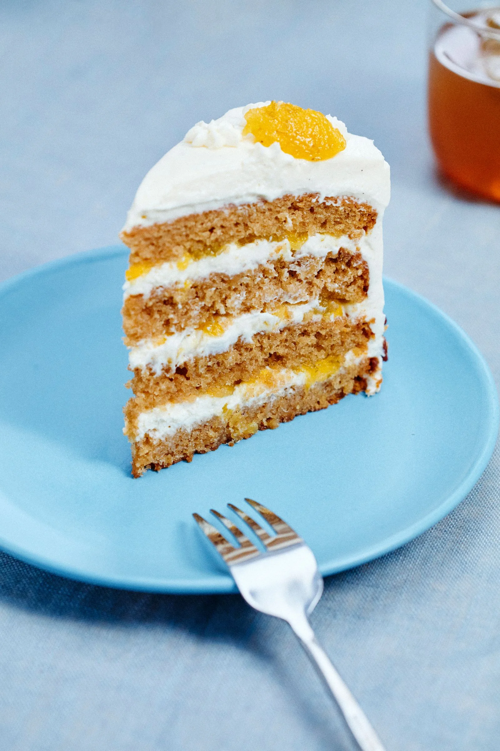 A slice of a fourlayer cake on top of a blue plate alongside a glass of tea.