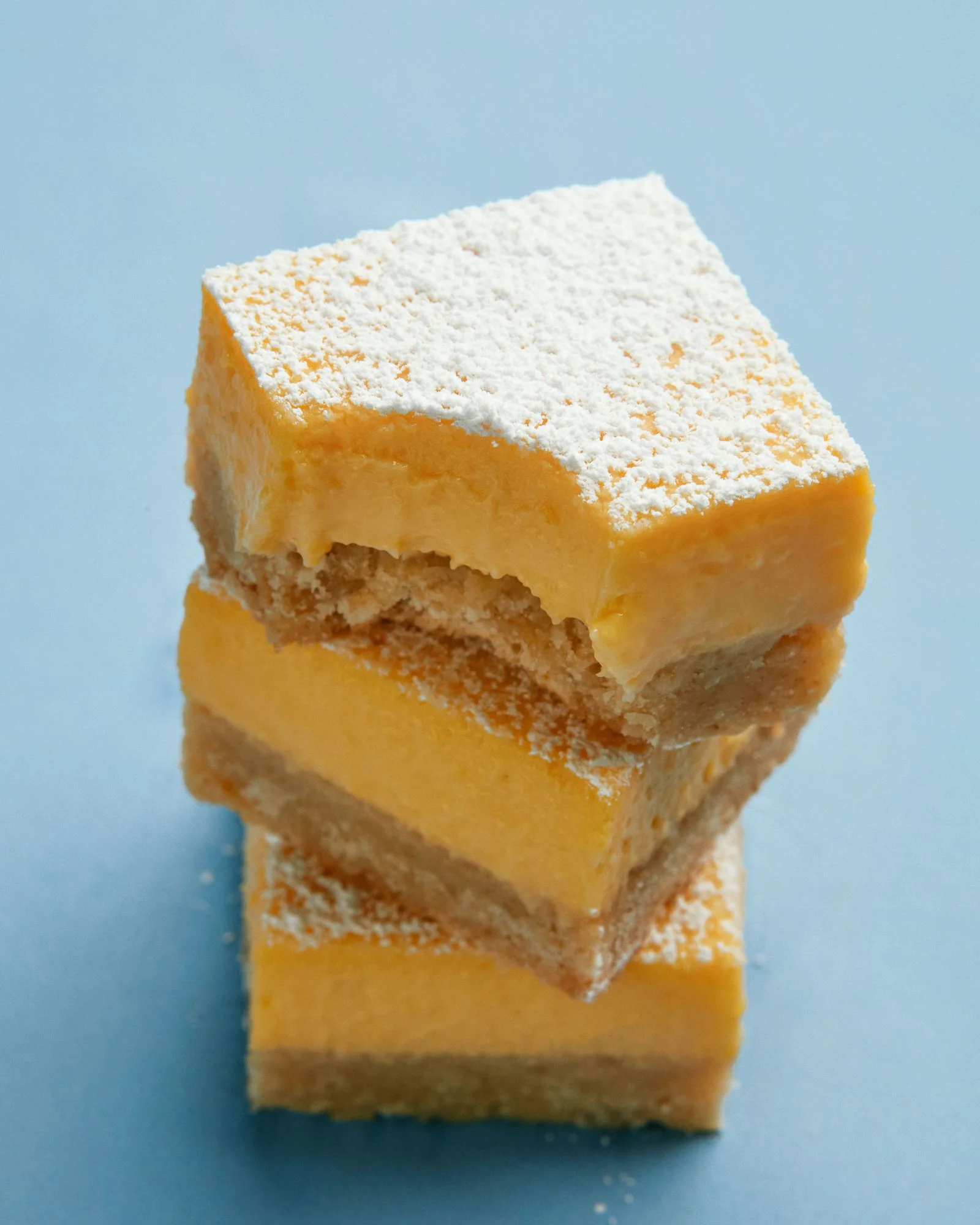 Three lemon bars dusted with confectioner's sugar one with a bite taken out.