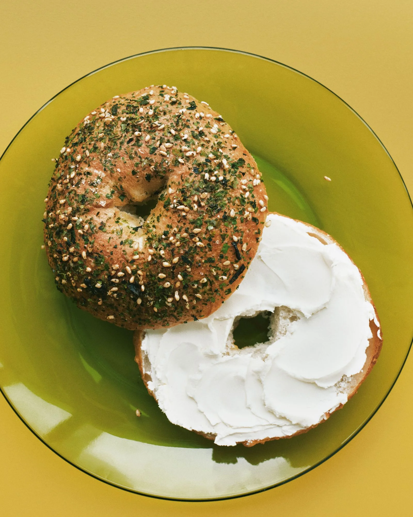 A bagel with furikake topping and cream cheese spread on a plate.