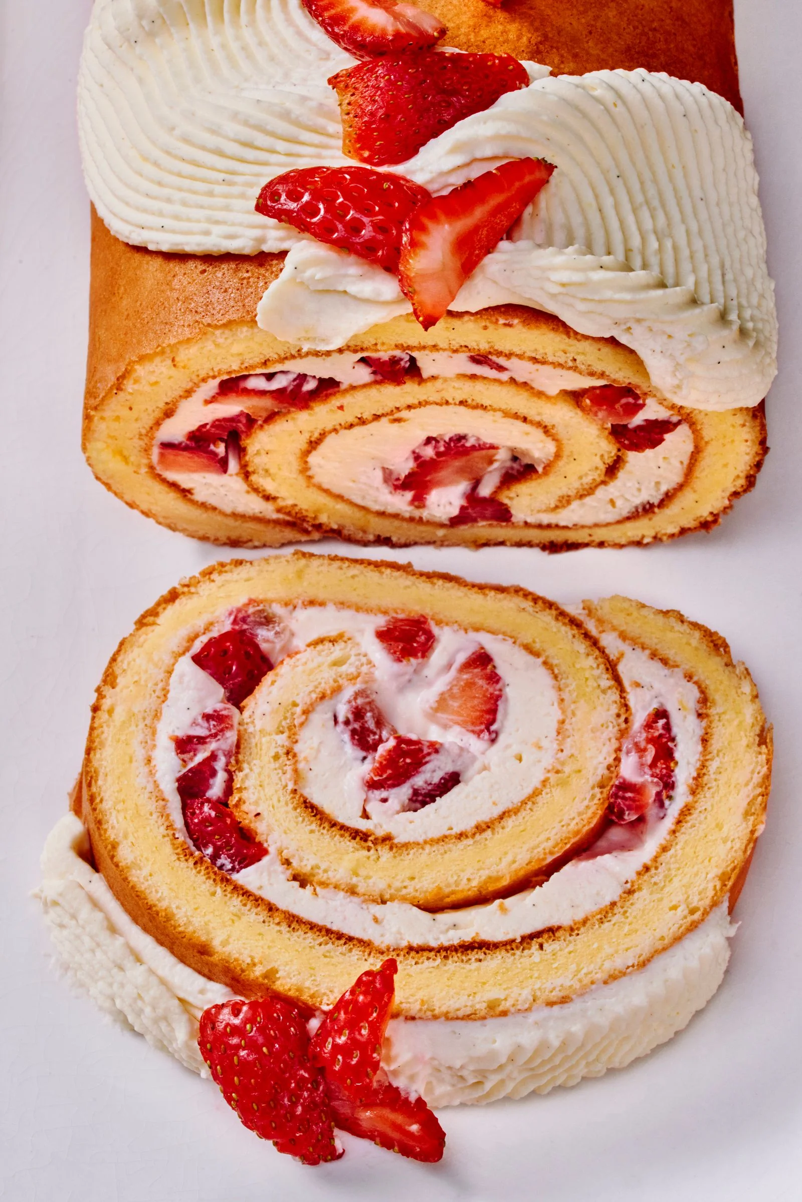 A cutinto strawberry swiss roll on a white platter seen from above.