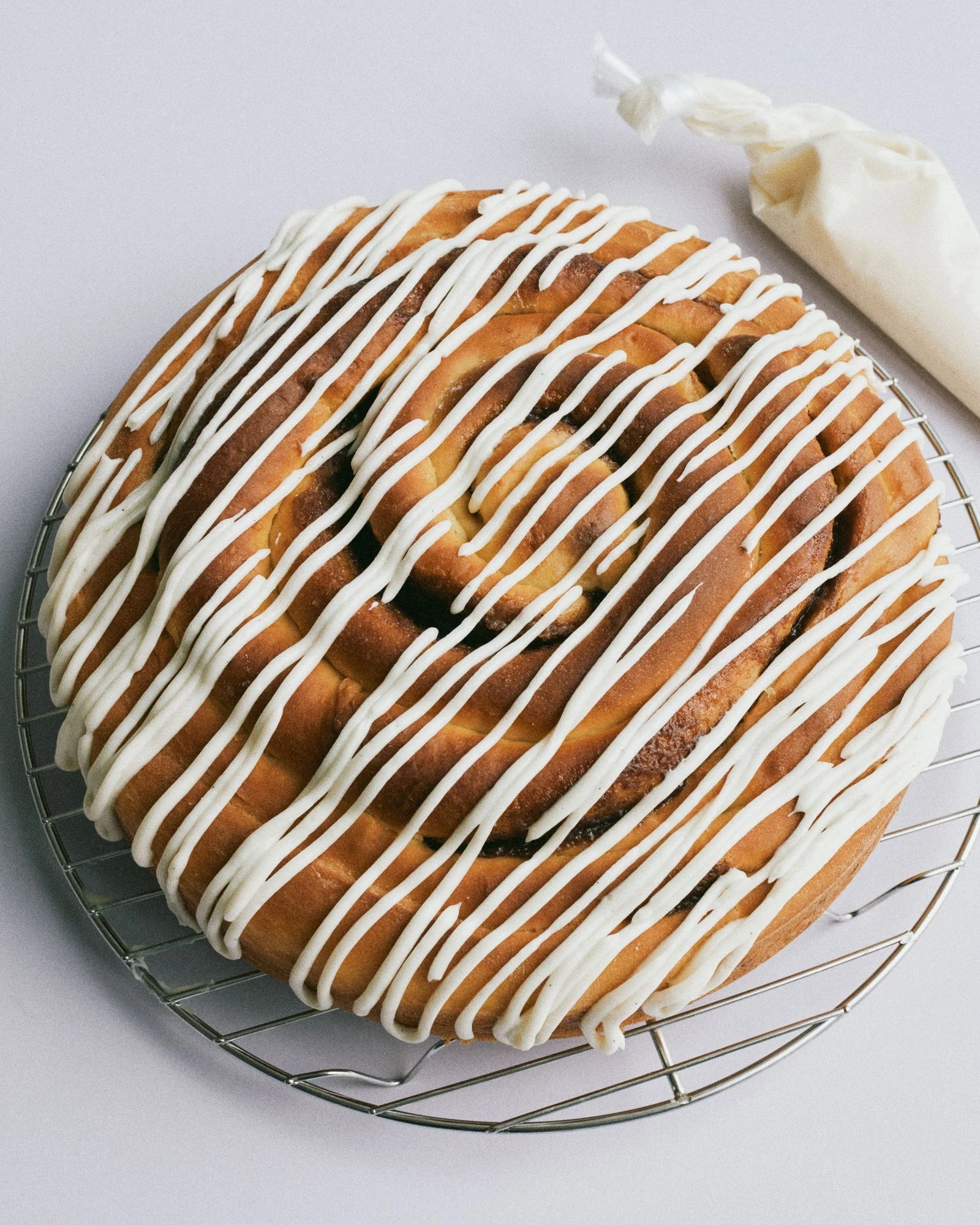 A giant cinnamon bun on a wire rack covered in icing.