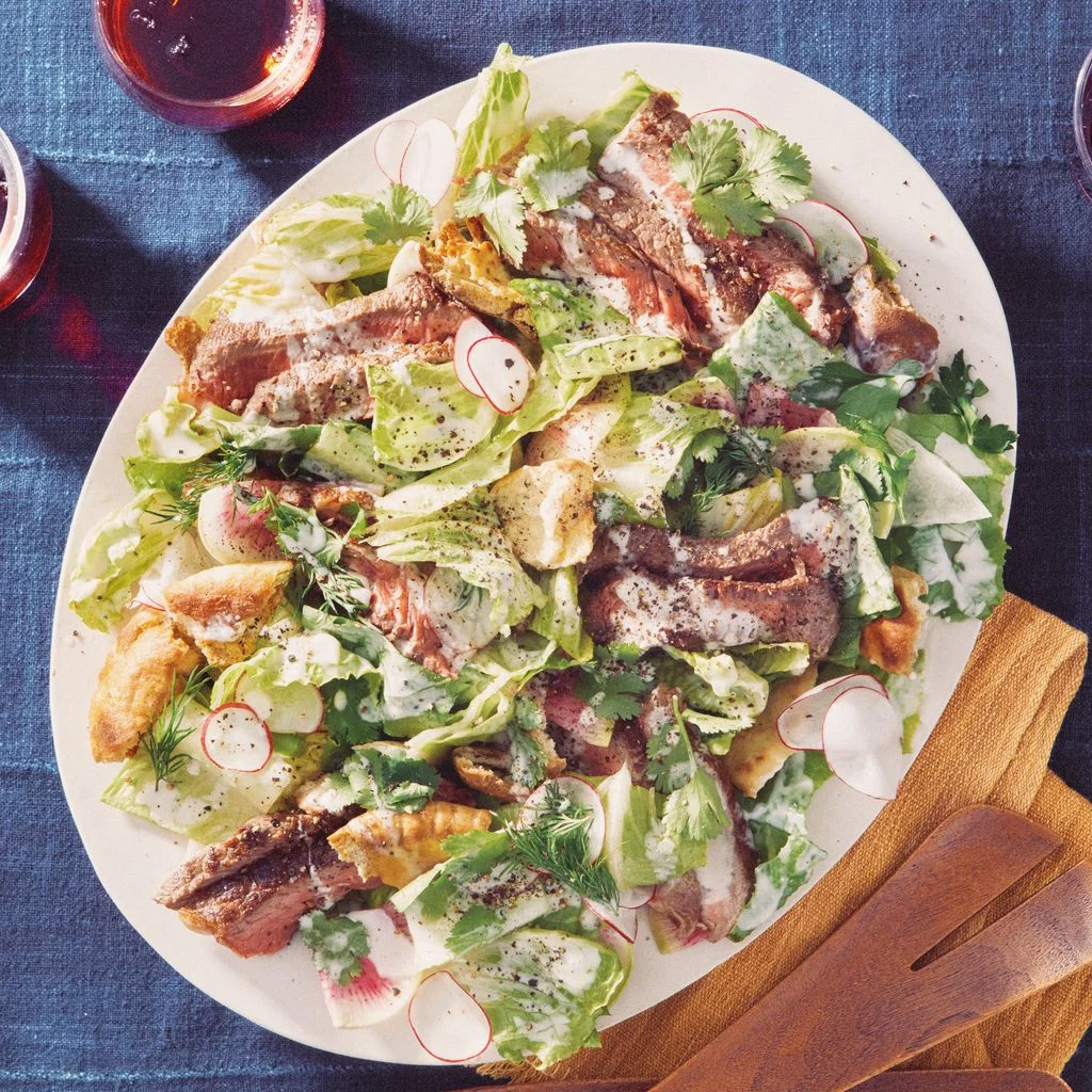 Platter of sliced ribeye steak salad with romaine lettuce toasted pita crumbled feta sliced radishes fresh herbs and...