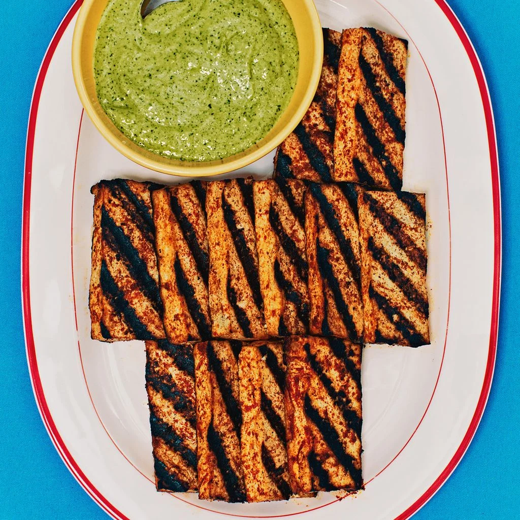 tofu on a white plate with a bowl of sauce on the left side