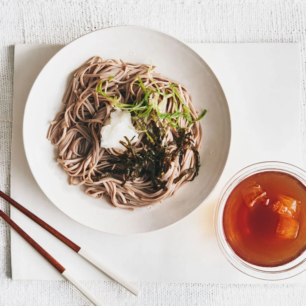 Soba noodles in a bowl with grated daikon thinly sliced scallions and shredded nori and served with wasabi and mentsuyu...