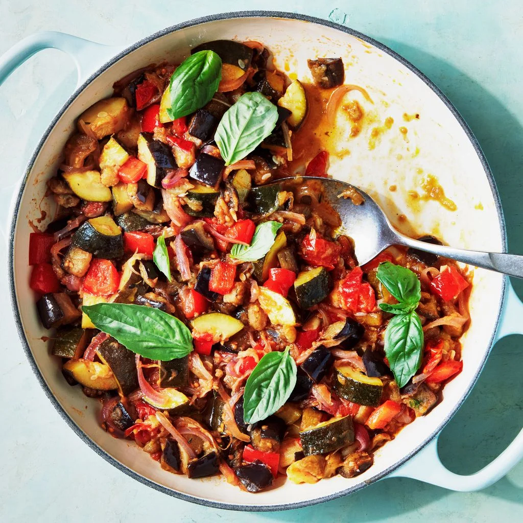 Onepot ratatouille with eggplant zucchini tomatoes red onion and bell pepper garnished with fresh basil in a shallow...