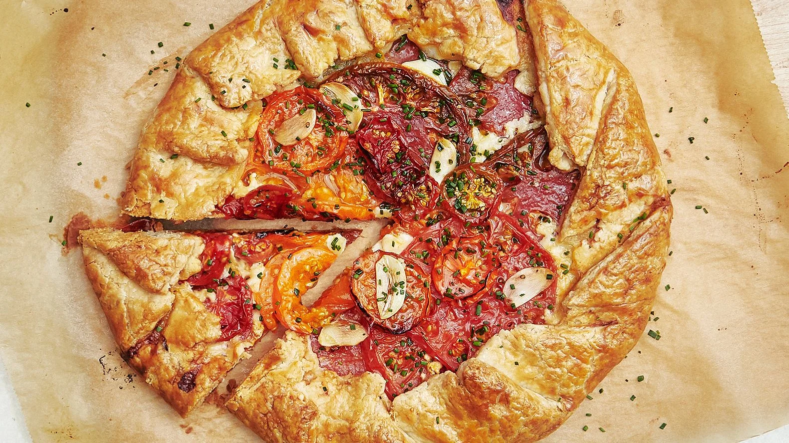 Overhead of a galette filled with caramelized tomatoes and garlic slices with one wedge cut out.