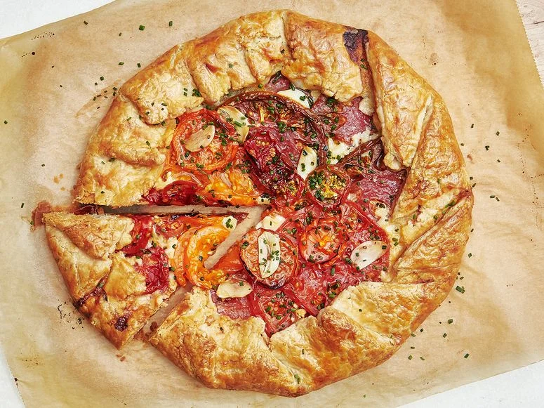 Overhead of a galette filled with caramelized tomatoes and garlic slices with one wedge cut out.