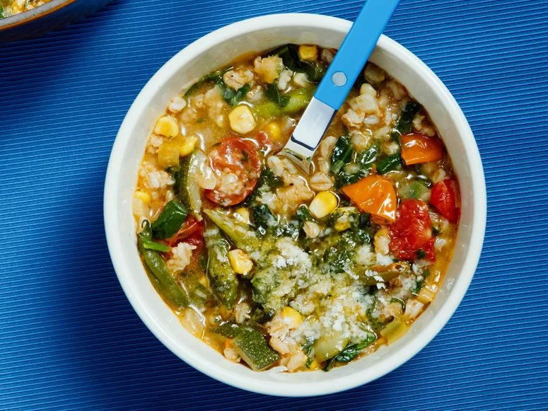 Two white bowls of minestrone alongside a large brown pot of the full yield.