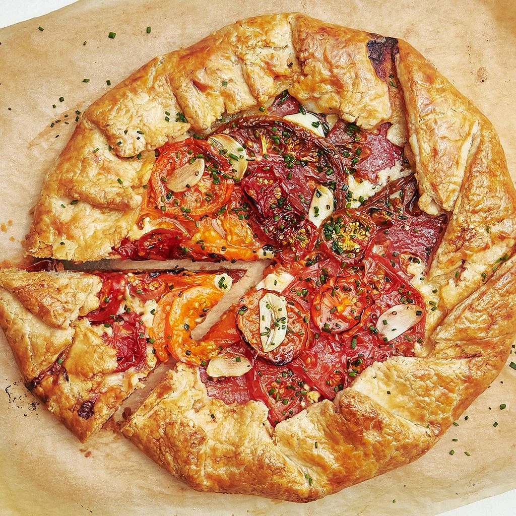 Overhead of a galette filled with caramelized tomatoes and garlic slices with one wedge cut out.