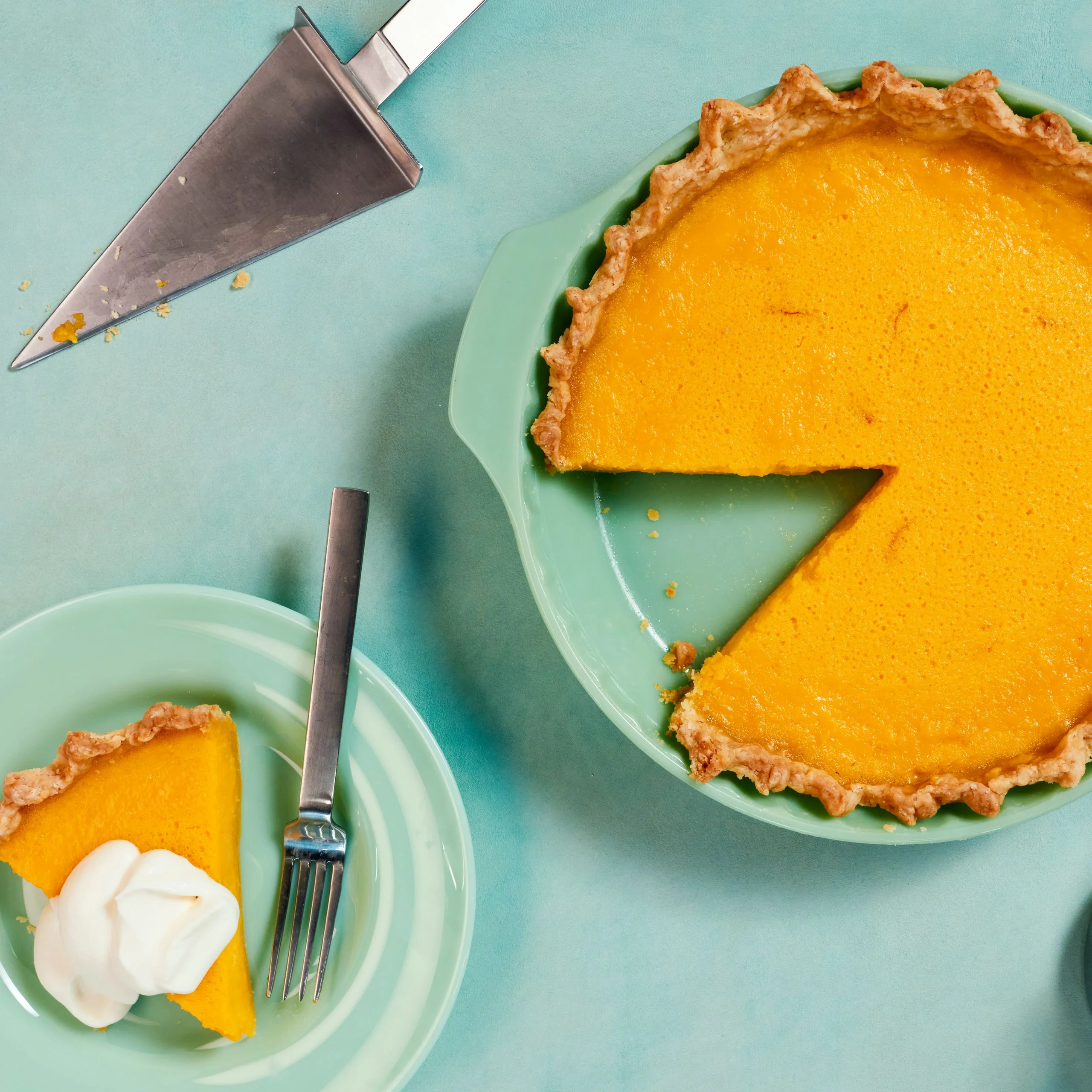 A goldenhued lemon buttermilk pie with saffron with one slice removed to a plate and topped with whipped cream.
