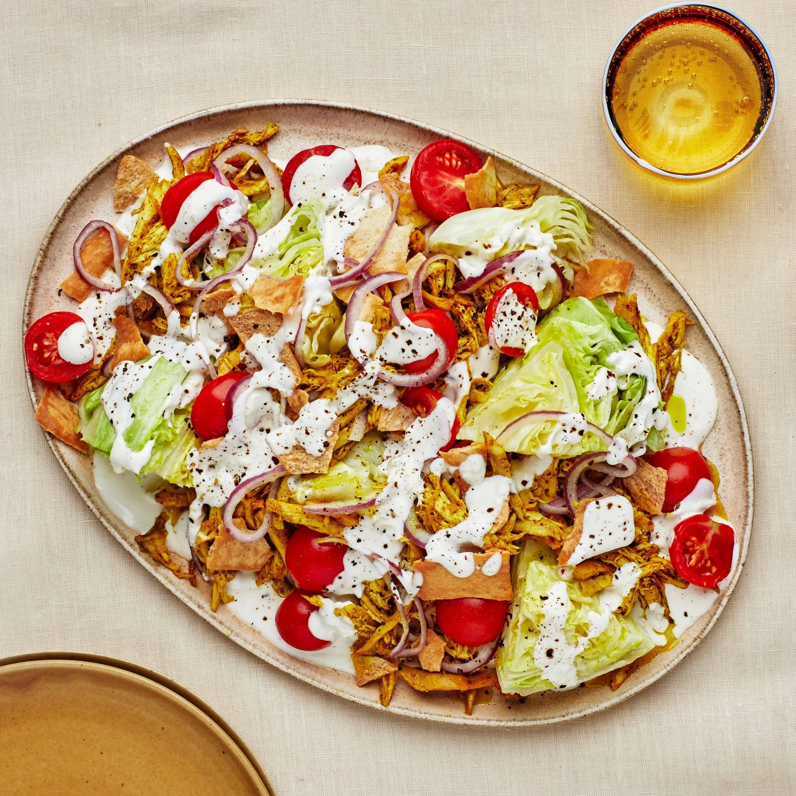 Salad on a platter with shredded chicken tomatoes iceberg and yogurt dressing drizzled on top.