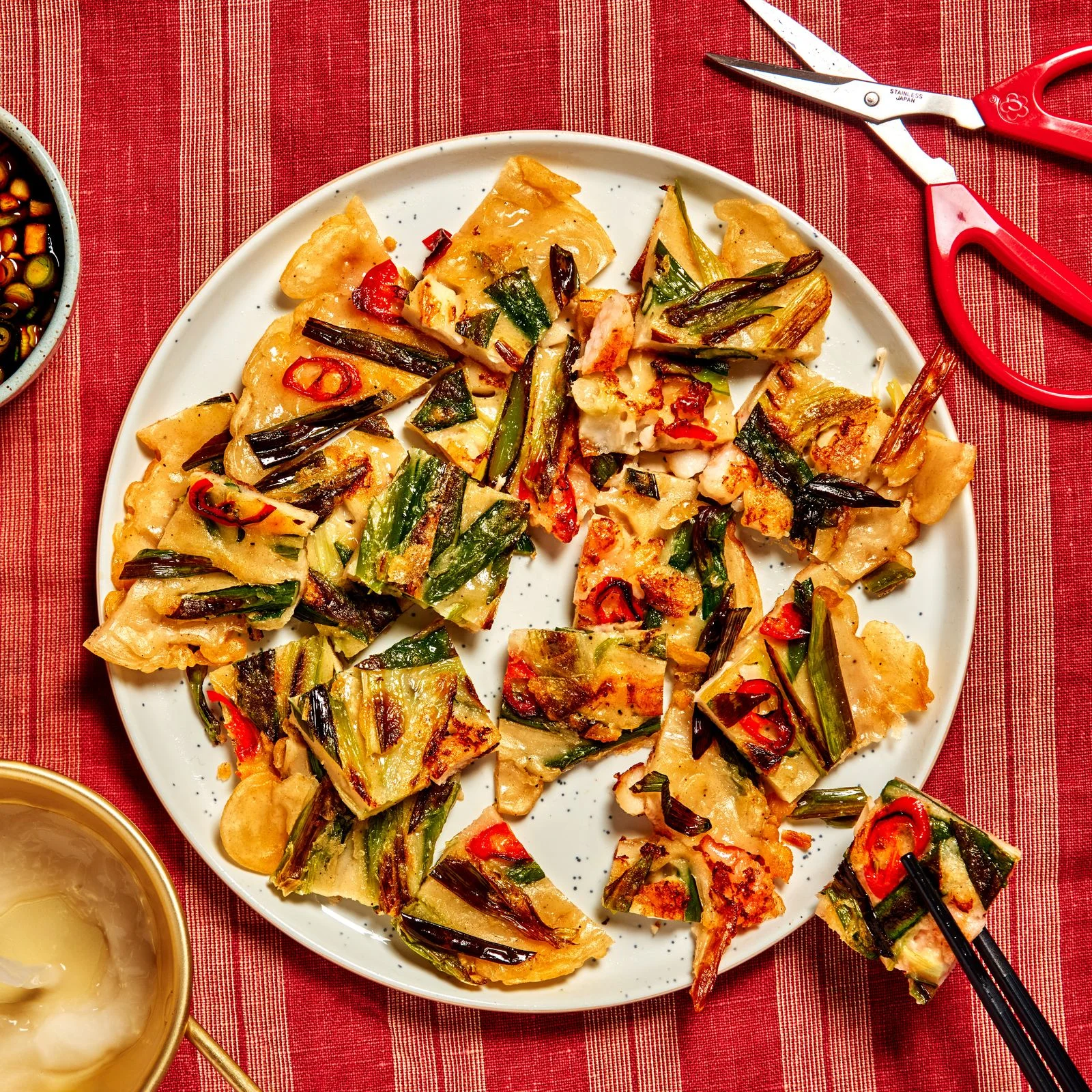 Haemul pajeon sliced into small bites on a white plate sitting on a striped tablecloth.