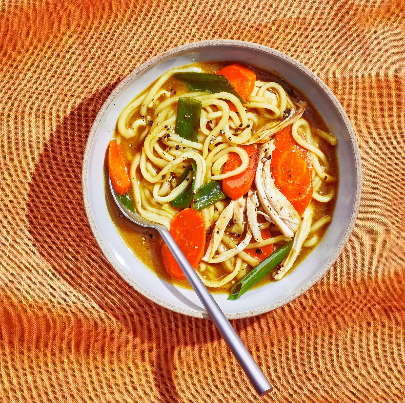 A bowl of Gingery Chicken Noodle Soup with carrot coins ramen noodles and scallions