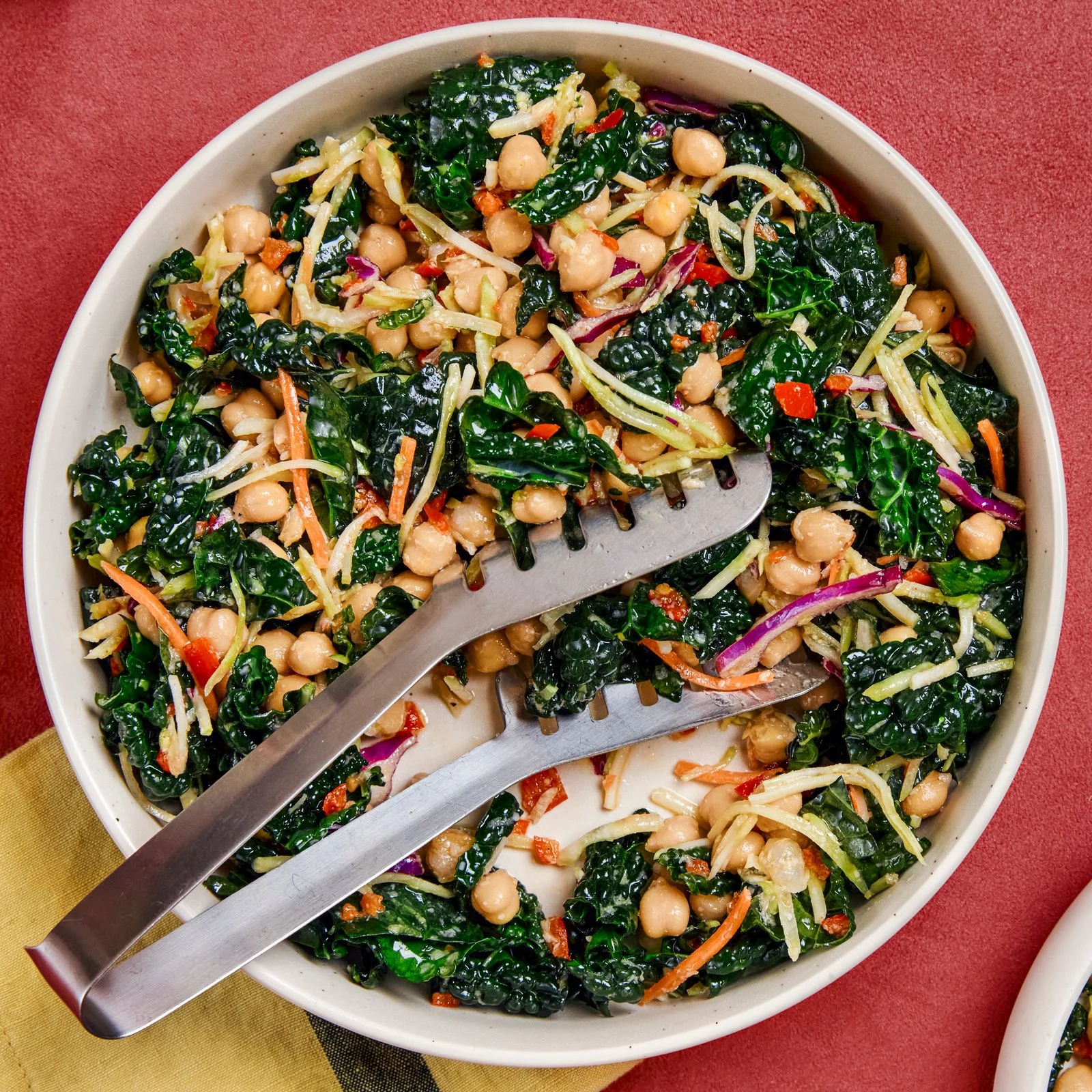 A serving bowl of chopped lacinato kale shredded carrots chickpeas red onions red bell peppers and shredded cabbage.