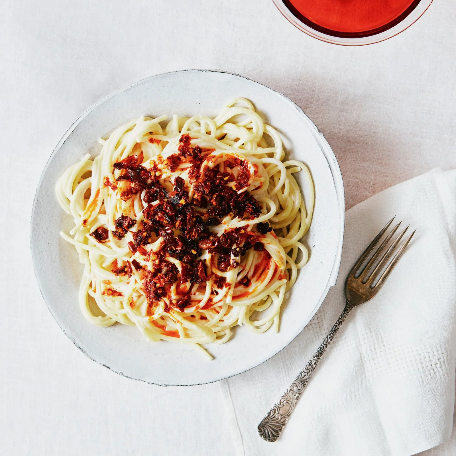 A shallow bowl of spaghetti topped with creamy chili crisp sauce.