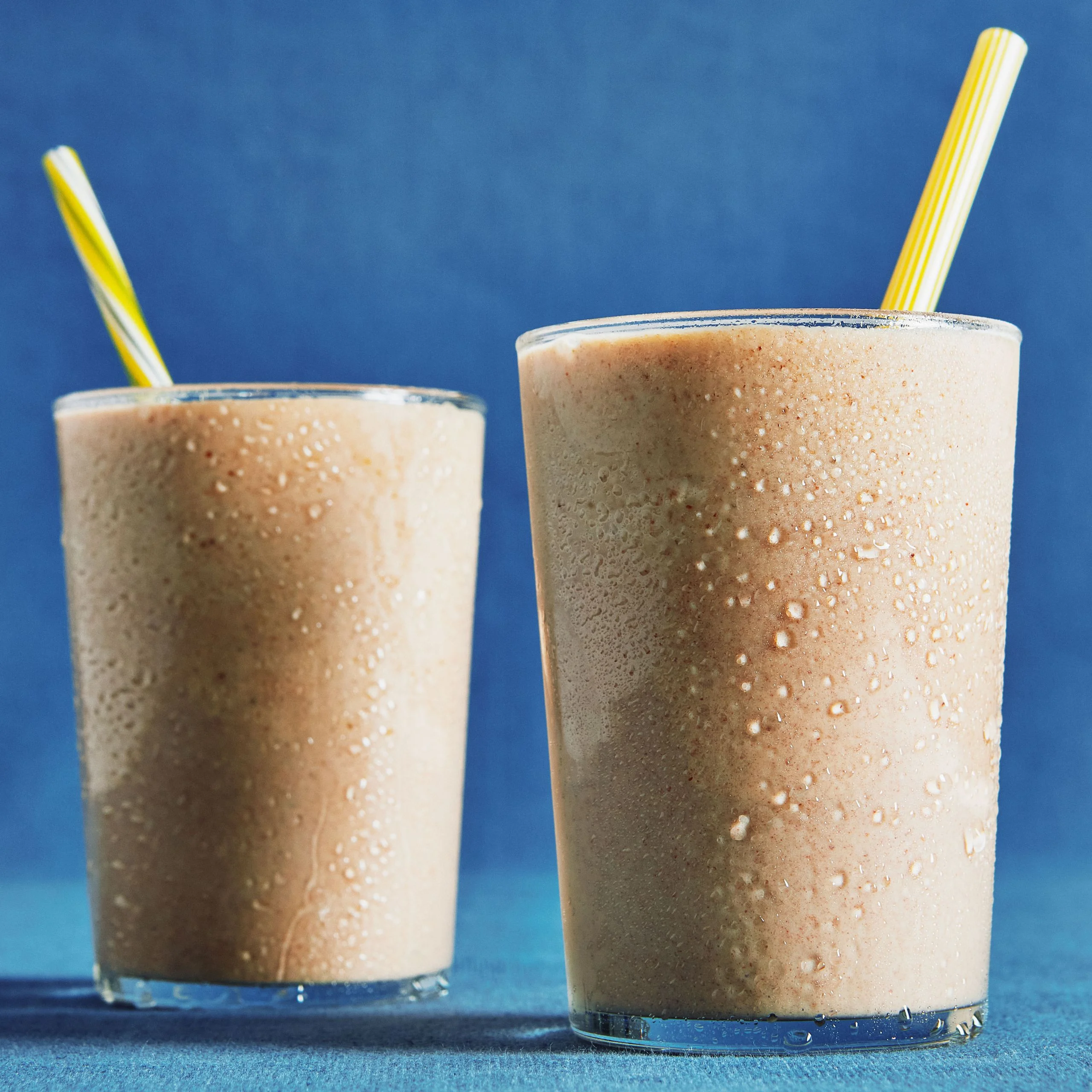 Two creamy Medjool date shakes with tahini and vanilla ice cream served in tall glasses with yellow straws.