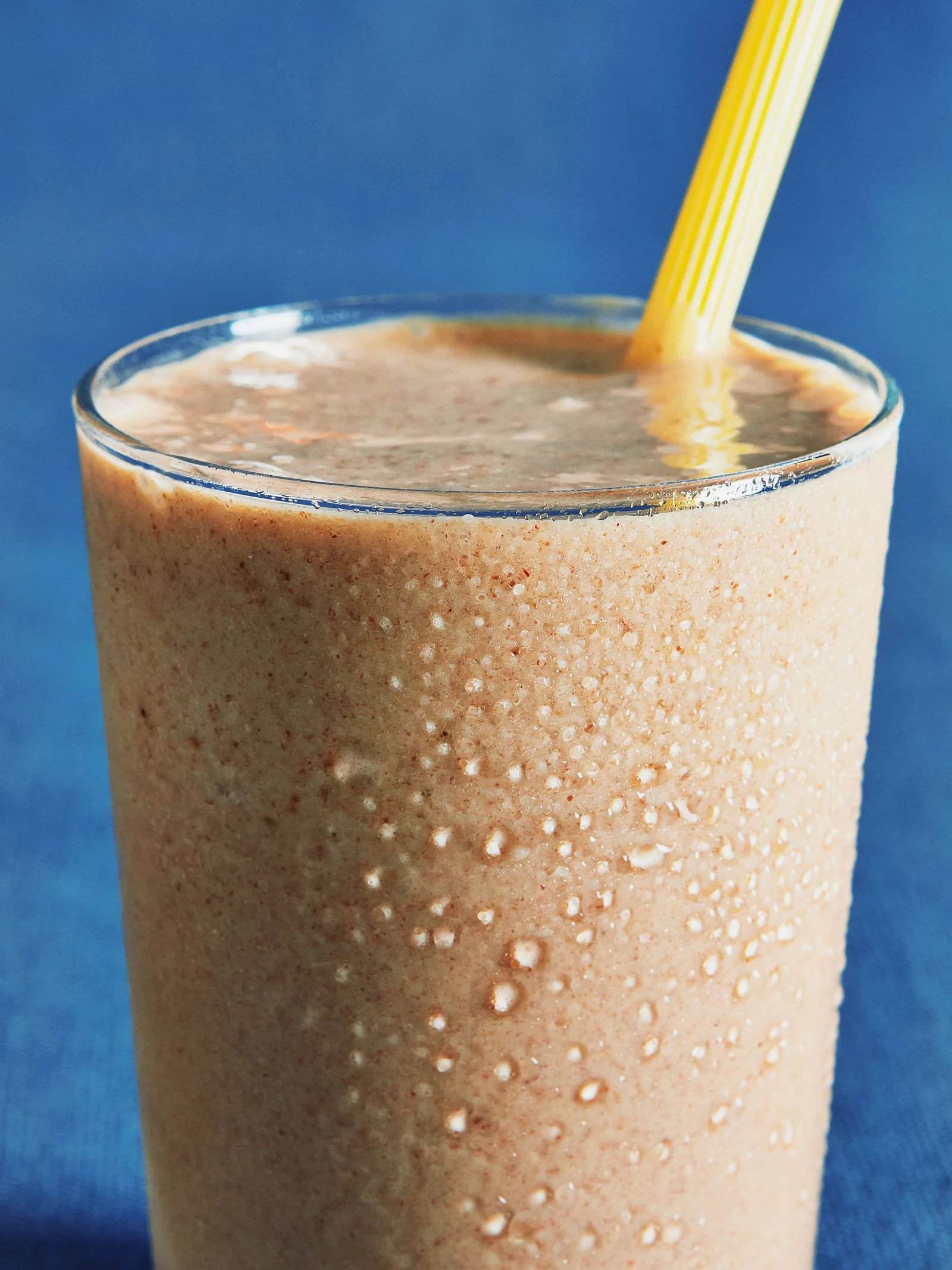 Creamy Medjool date shake with tahini and vanilla ice cream in a glass with a yellow straw.