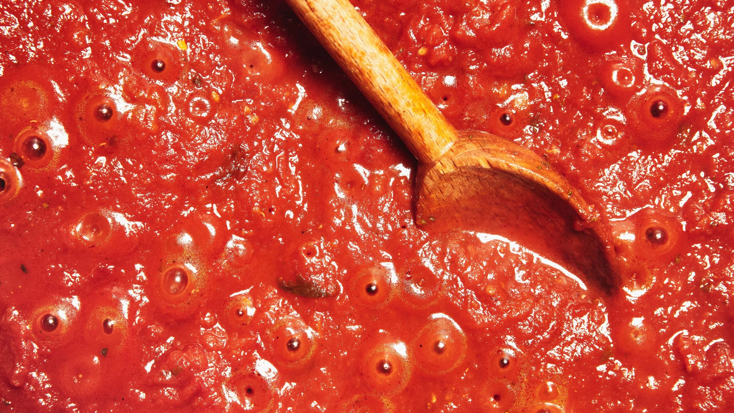 Marinara bubbling away in a pot with a wooden spoon.