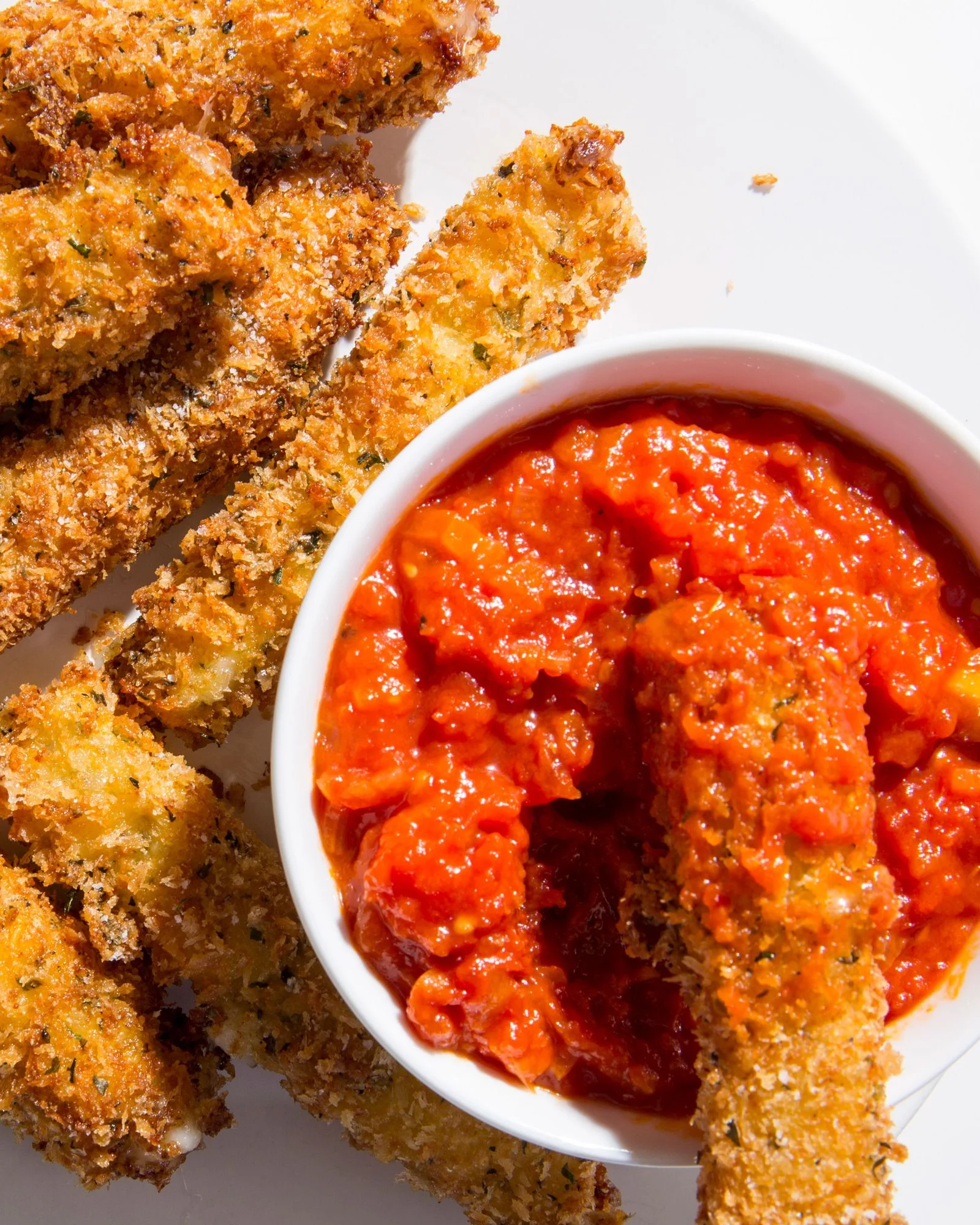 A platter of breaded fried mozzarella sticks with a sidecar of marinara for dipping.