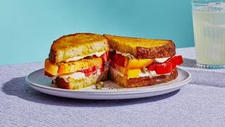 A sandwich with thick slices of tomato curry mayonnaise and toasted sourdough bread sliced in half on a plate.