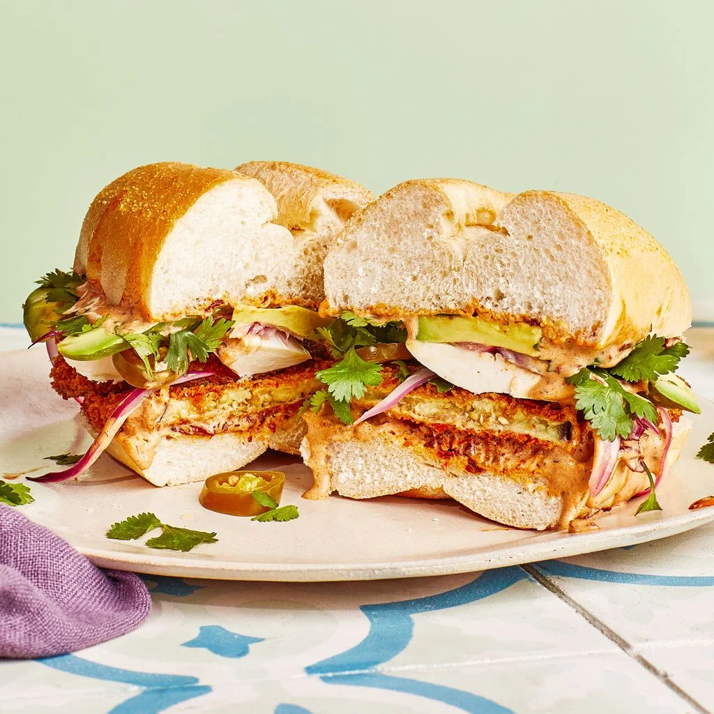 Eggplant cutlet sandwich with a beer against a green wall.