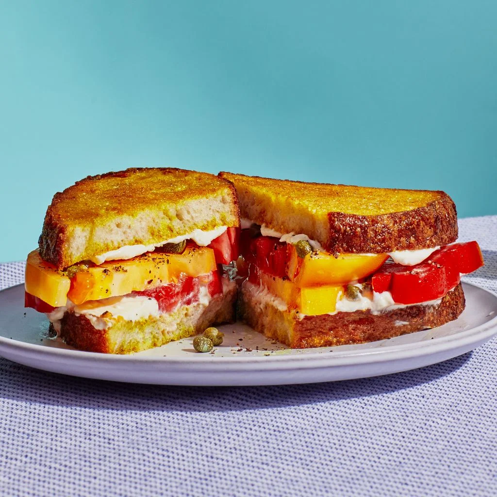 A sandwich with thick slices of tomato curry mayonnaise and toasted sourdough bread sliced in half on a plate.