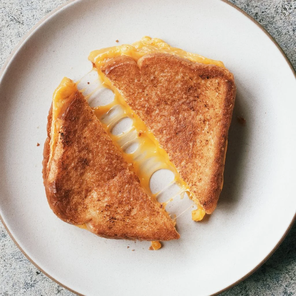 A halved grilled cheese on a plate with melting cheese.