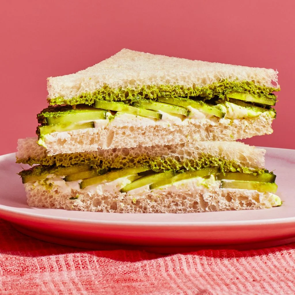 Two halves of a diagonally sliced cucumber sandwich stacked on a plate.