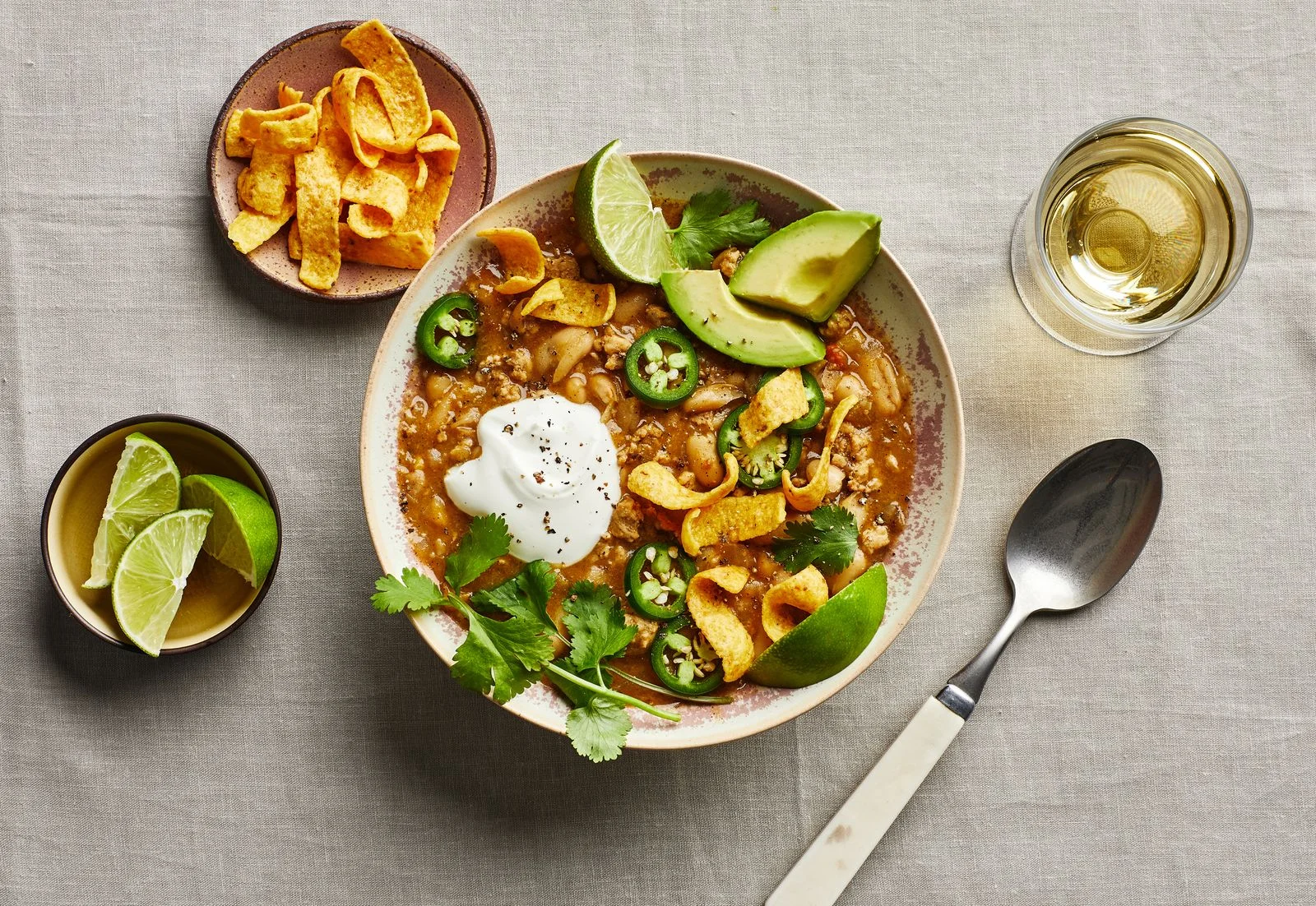Bowl of white chicken chili topped with Fritos cilantro jalapeño avocado and sour cream.