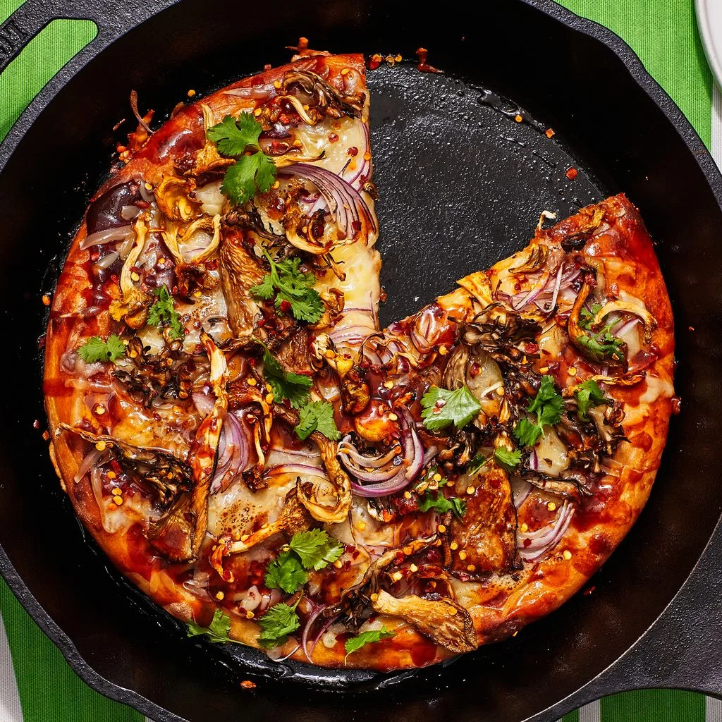 Barbecue mushroom pizza in a cast iron skillet on a green striped tablecloth.