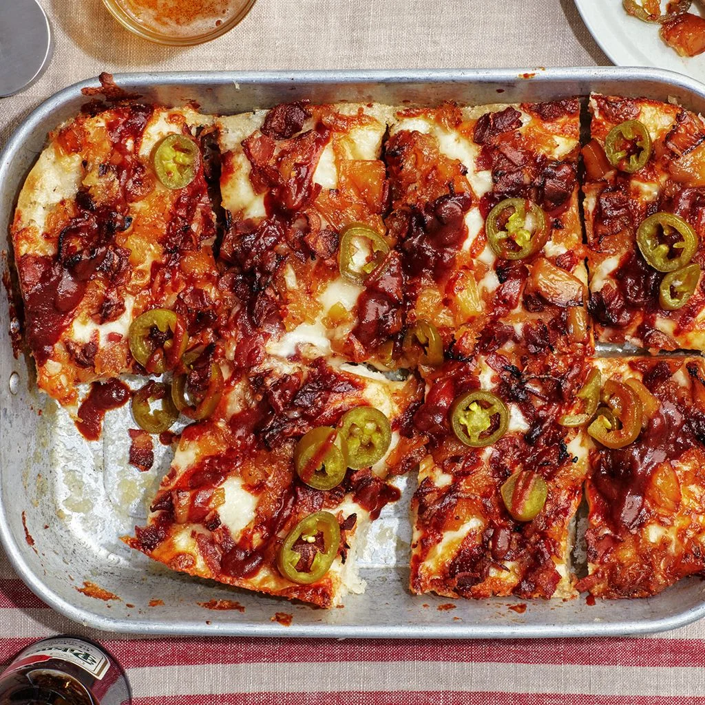 A Hawaiian Detroitstyle pizza with barbecue sauce beef bacon pineapplea nd pickled jalapeños.