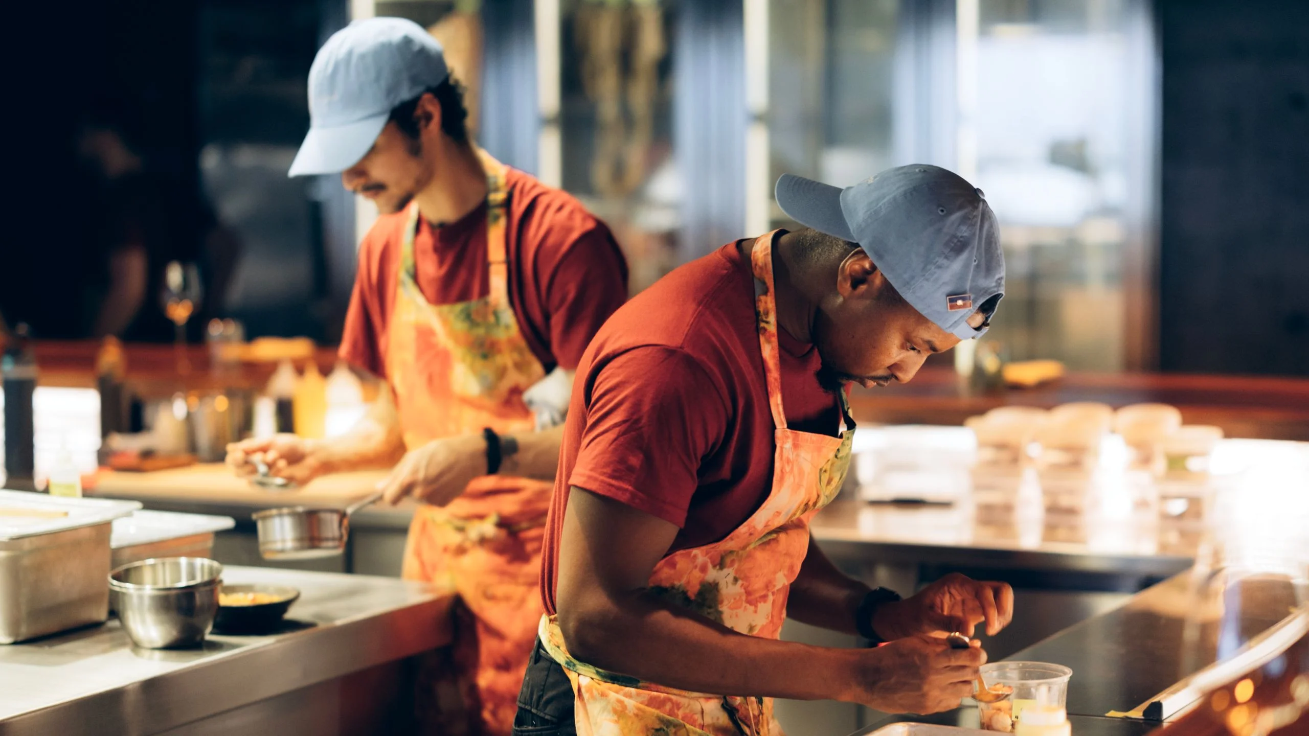 Two people in a sparsely lit restaurant kitchen prep dishes sidebyside.