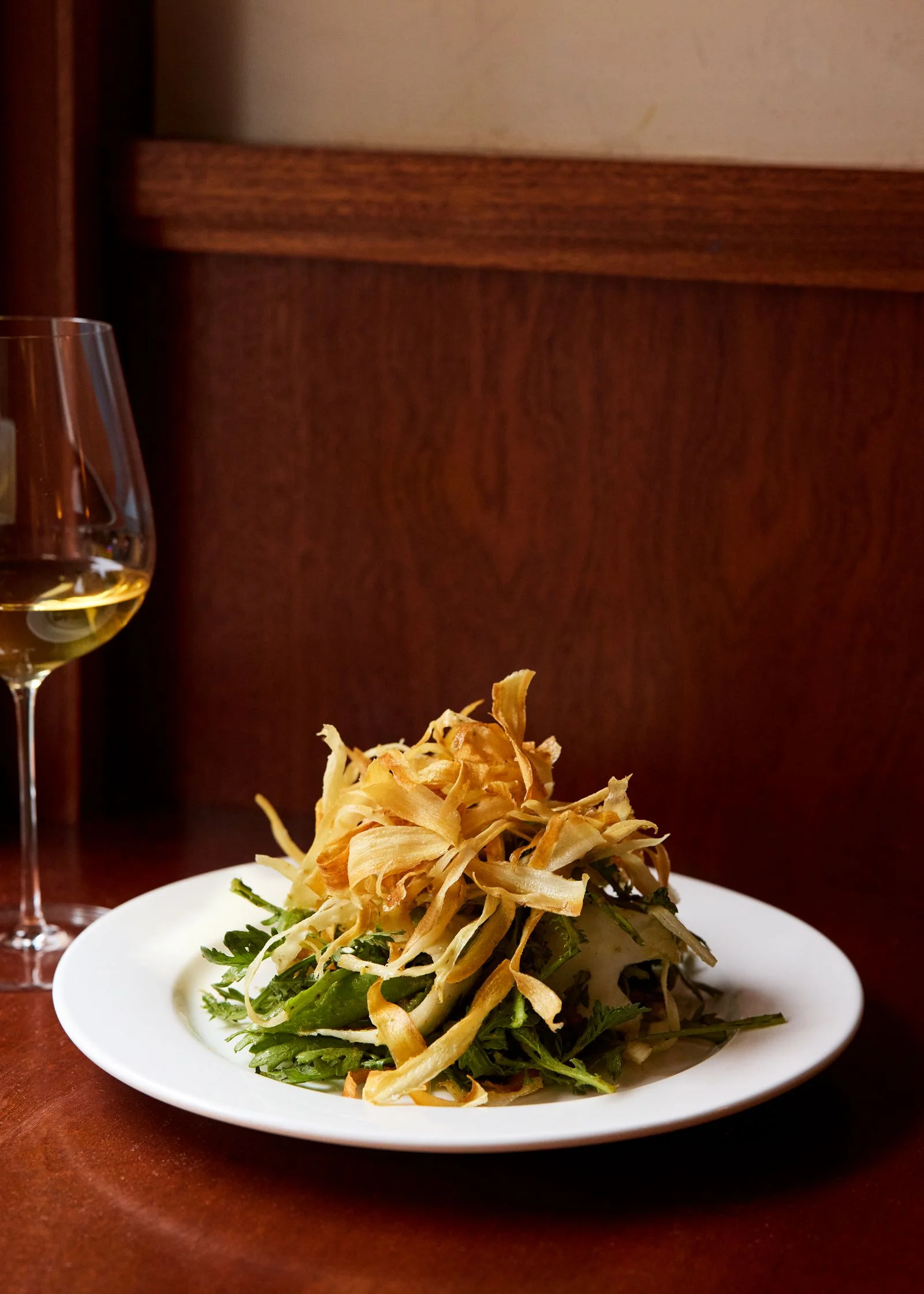 A chrysanthemum leave and shaved burdock root salad with a glass of white wine at Lei in Chinatown New York City.