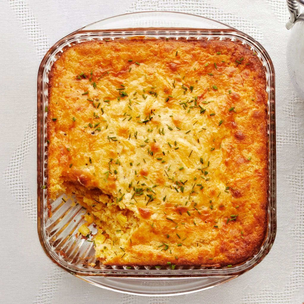 Corn pudding in a square casserole dish with one scoop removed.