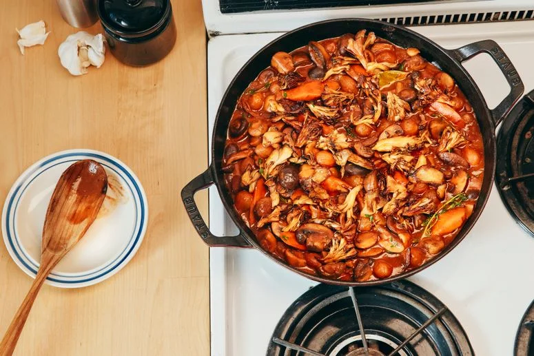 A cast-iron skillet filled with mushroom bourguignon resting on a white and black stovetop.