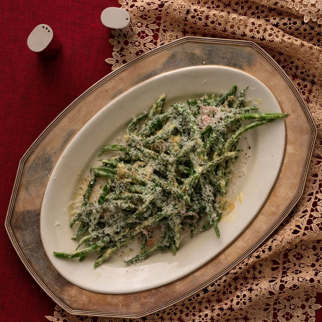 A platter of green beans dressed in parmesan vinaigrette against a neutral lace runner and maroon tablecloth.