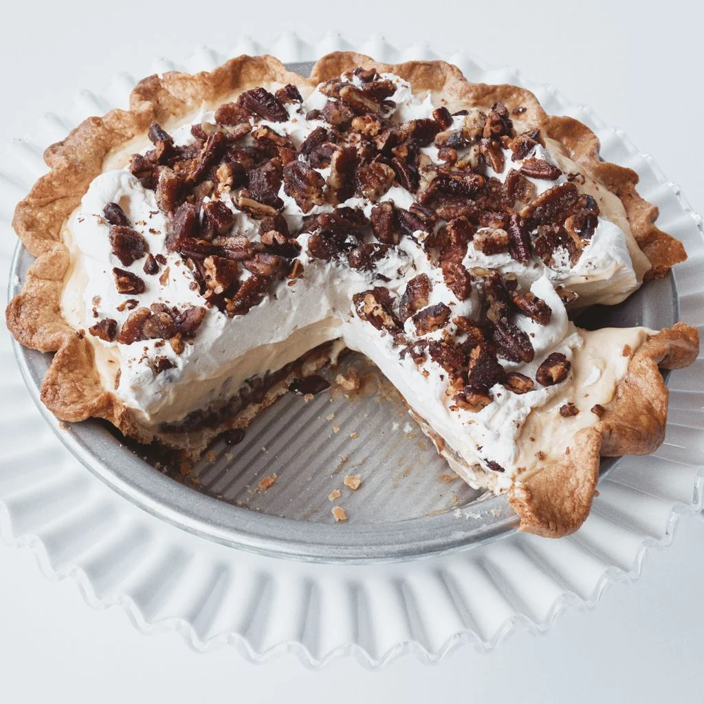 A pecan cream pie with layers of gooey chopped pecans brown sugar custard and whipped cream topped with candied pecans.