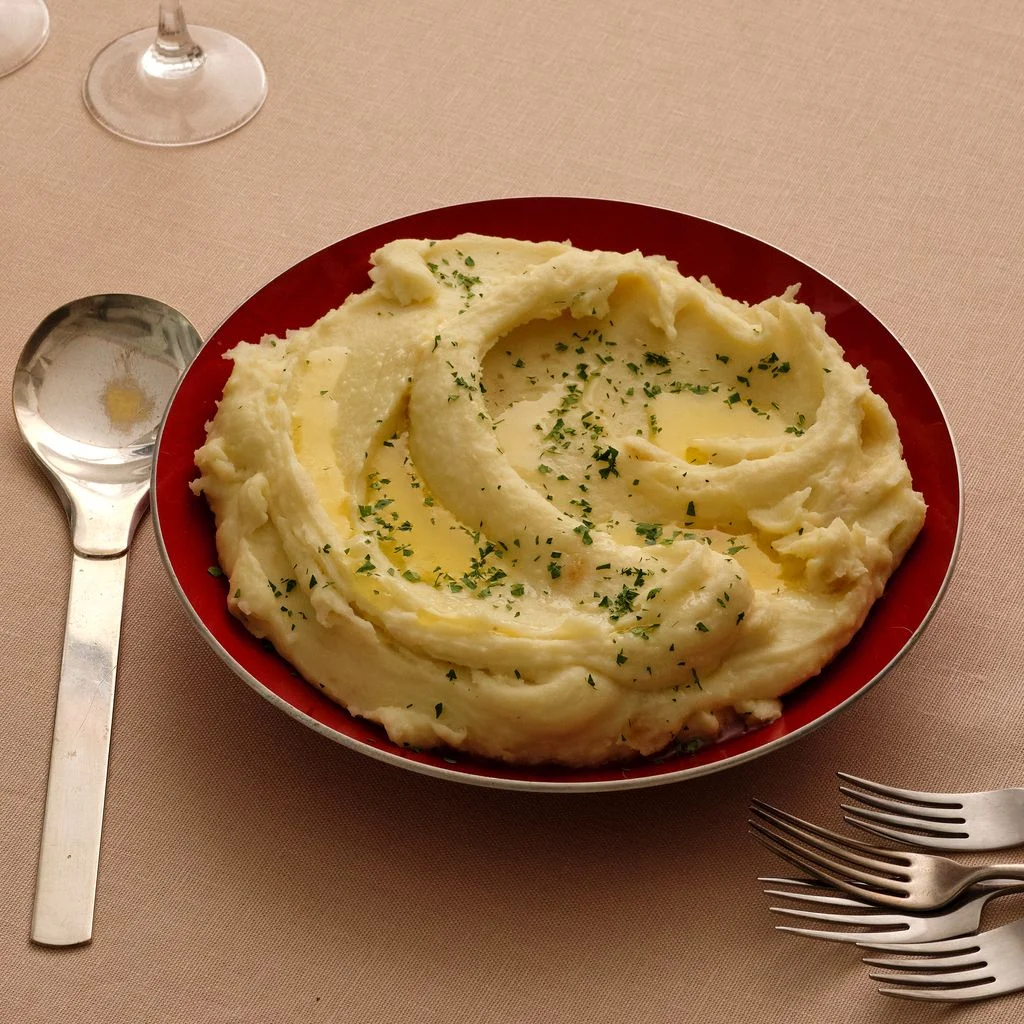 A red bowl filled with creamy mashed potatoes with buttery wells.