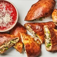 Three broccoli-stuffed calzones, halved and set on a platter with a bowl of marinara for dipping.