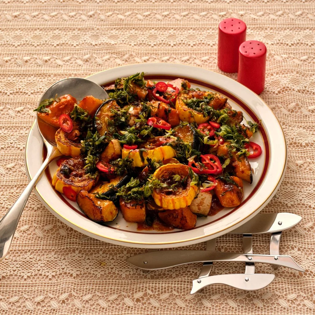 A brownrimmed white ceramic plate filled with round cuts of various squash roasted and speckled with peppers.