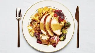 A full Thanksgiving plate with sliced turkey breast topped with gravy roasted brussels sprouts stuffing radicchio salad...