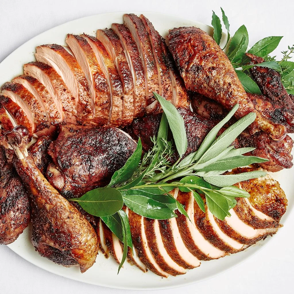 A carved Thanksgiving turkey on a platter with sage and thyme stems and fresh bay leaves sprigs tucked in for garnish.