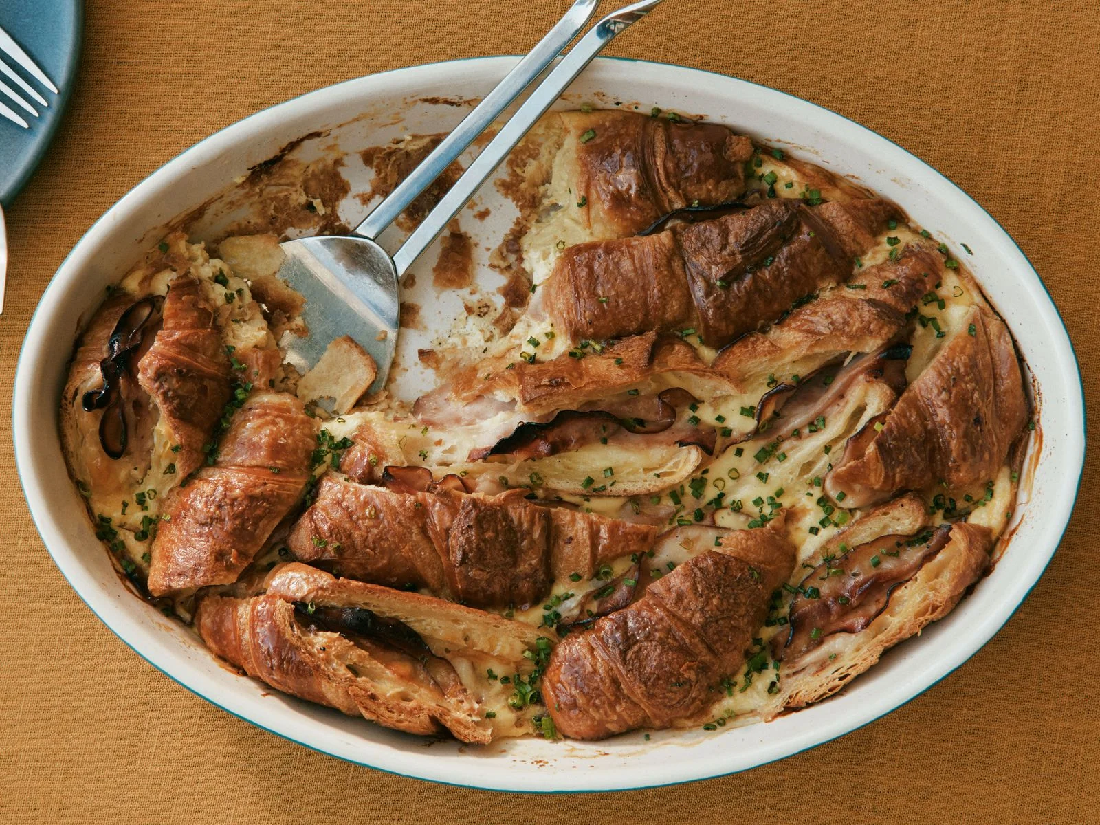 Ham and cheese croissant sandwiches baked into a cheesy casserole and topped with chopped chives.