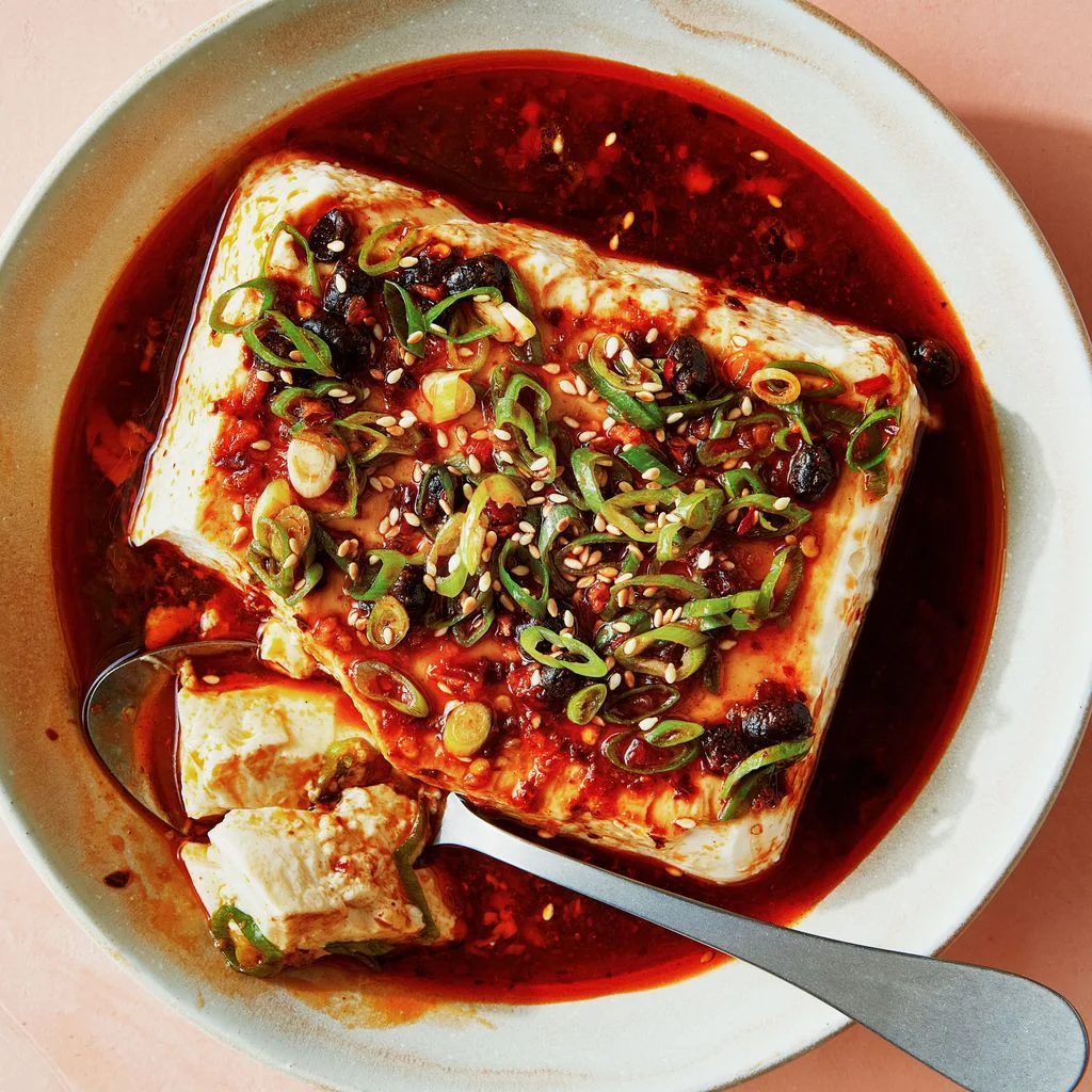 A block of silken tofu in a shallow bowl topped with chili crisp and sliced scallions.