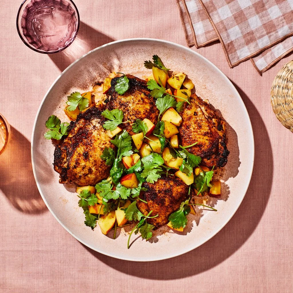 Cajunspiced chicken thighs topped with fresh peach salsa on a dinner plate beside summer cocktails